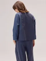 Camisa de manga larga con diseño bicolor en tonos tierra. Presenta un panel frontal y trasero en color beige, contrastado con mangas de un tono marrón más oscuro y textura satinada. Posee cuello redondo y corte recto.