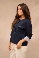 Campera azul marino de corte recto, con cuello redondo, cierre frontal con botones oscuros, bolsillos frontales con solapa en el pecho y mangas largas con vuelta estampada a rayas.