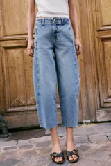 Jeans de tiro alto con corte barrel, pernera holgada que se estrecha hacia el tobillo y bajo deshilachado. Presenta costuras verticales decorativas en el frente y cierre frontal con cremallera y botón.
