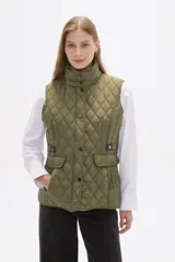 Chaleco acolchado de diseño capitoneado en color verde militar, con cuello alto, cierre frontal con botones a presión y bolsillos laterales con solapa y detalles en contraste.