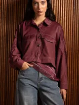 Campera corta de diseño liviano en color bordó, con costuras a la vista en color contrastante, cierre frontal con botones dorados y bolsillos frontales con solapa.