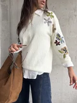 Sweater de punto color natural con cuello redondo y mangas largas, decorado con bordados florales multicolores en las mangas y hombros.