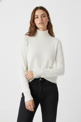 Polera de tejido de punto fino, color blanco, con cuello alto y mangas largas ajustadas.