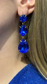 Aros colgantes de diseño articulado con tres cristales azules facetados en engaste dorado. Presenta un cristal circular superior, uno ovalado central y uno en forma de gota en la parte inferior.