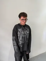 Remeron oversize de algodón pesado color negro con estampado gráfico en serigrafía gris en el frente y en ambas mangas. Presenta cuello redondo y grifa de la marca en el puño.