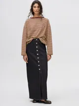 Falda midi de denim color mostaza, con tiro medio, corte recto, cierre frontal de botones metálicos y tajo delantero en el ruedo con terminación deshilachada.
