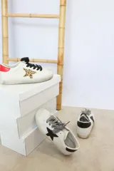 Zapatillas bajas blancas con cordones negros, estrella de animal print y detalle rojo en el talón.
