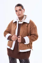 Campera de gamuza sintética color tostado con interior y detalles de corderito blanco. Presenta cierre frontal, cuello solapa, puños de tejido acanalado y correas ajustables con hebilla en los laterales.