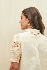 Camisa color crema o amarillo muy pálido, con cuello clásico y mangas cortas abullonadas que presentan bordados calados florales (broderie anglaise).