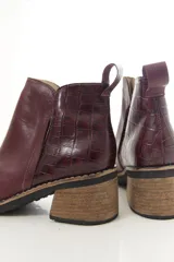 Botinetas de cuero vacuno color bordó, con diseño urbano y elegante. Presentan un detalle texturizado tipo cocodrilo en la parte trasera, taco bajo de madera y puntera cuadrada.