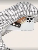 Bolso de mano tipo baguette, color negro, confeccionado en malla metálica con efecto lentejuelas o escamas. Tiene un asa única curva y cierre de cremallera en la parte superior.