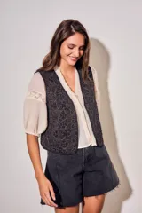 Chaleco sin mangas de corte al cuerpo, color negro con bordados florales en hilo contrastante. Presenta un diseño abierto con terminaciones reforzadas.