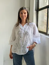 Camisa blanca de corte holgado y manga larga, con delicados bordados florales en tono gris claro en el frente.