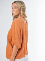 Remerón tipo poncho color naranja confeccionado en lino italiano, con escote en V y bolsillos laterales.