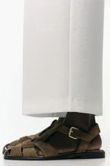 Zapato plano tipo cangrejera de mujer, color verde militar, confeccionado en serraje (gamuza). Presenta tiras trenzadas en la parte delantera y cierre con hebilla metálica en el tobillo.