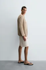 Cardigan de punto grueso color beige, con cuello pico, manga larga y cierre frontal de botonadura.