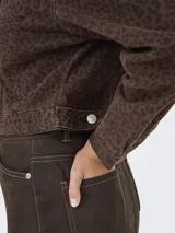 Campera trucker de twill color marrón con estampado animal print de leopardo en negro. Cuenta con cuello clásico, cierre de botones frontales, puños abotonados y bolsillos en el pecho.