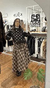 Pollera midi de corte amplio con estampado escocés en tonos marrones. Presenta un diseño distintivo con un sistema de cierre y ajuste en la cintura que simula puños de camisa anudados.