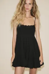 Vestido corto negro de gasa con escote recto y tirantes finos ajustables. El corpiño tiene fruncido elástico y el ruedo es escalonado con volados. Presenta un detalle de encaje a tono en el borde del escote.
