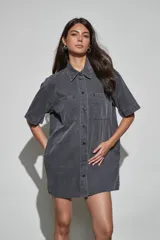 Vestido corto de denim azul oscuro, con cuello camisero, mangas cortas, cierre frontal de botones y dos bolsillos en el pecho.