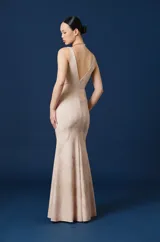 Vestido largo color beige, con escote en V, sin mangas y silueta ajustada que se ensancha levemente hacia el ruedo.