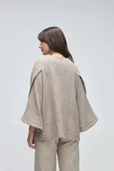 Capa de lana fina sin teñir, con diseño de corte amplio y mangas tipo kimono. Presenta cierre frontal mediante tres alamares de cuero en tono marrón.