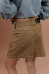 Minifalda de gabardina color tostado, de tiro medio con bolsillos delanteros y traseros, presillas para cinto y cierre frontal con botón metálico.