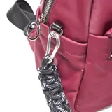 Mochila de diseño urbano en color bordó, confeccionada en material textil. Cuenta con compartimento principal con cierre, bolsillo frontal con cierre, manija superior y detalle de llavero trenzado en blanco y negro. Incluye logo circular de la marca en la parte inferior.