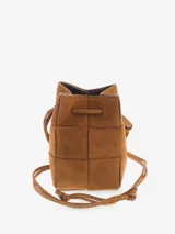 Cartera tipo bucket de diseño compacto, confeccionada en cuero con textura gamuzada. Presenta un diseño trenzado, cierre mediante lazo ajustable y correa larga para llevar al hombro o cruzada.