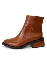 Bota corta de cuero vacuno color suela, con diseño de punta cuadrada y taco de madera con acabado veteado. Presenta costuras visibles en el empeine y cierre lateral interno.