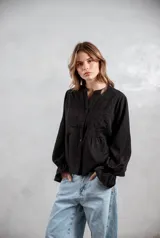 Camisa negra de corte holgado con detalles de bordado tipo broderie en el pecho y mangas largas con puños acampanados.