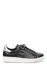 Deportivo de cuero negro con cordones, suela blanca y detalle metalizado en el talón.