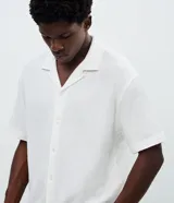 Camisa de corte boxy fit, color blanco, con cuello bowling, cierre frontal con botones y manga corta. Confeccionada en tejido de algodón con textura jacquard.
