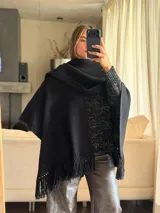 Ruana tejida a mano en punto arroz, color negro, con flecos en los bordes inferiores.