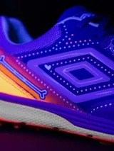 Championes de fútbol 5 Umbro Bump, color violeta con detalles en naranja y blanco. Presentan un diseño texturizado en la puntera y el logo de Umbro en los laterales.