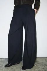 Pantalón de tiro medio con diseño de raya diplomática, corte wide leg y detalle de pinzas en el delantero. Cuenta con cintura con trabillas, bolsillos laterales y cierre frontal con cremallera, botón y ganchos metálicos.