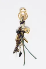 Llavero de diseño náutico compuesto por cabos trenzados en tonos beige, marrón y violeta, con herrajes metálicos dorados y dije cuadrado con logo de la marca esmaltado.