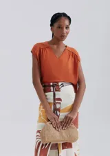 Blusa naranja sin mangas con escote en V y detalle de frunces en los hombros.