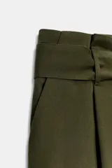 Pantalón cargo de tiro medio en color verde militar. Presenta bolsillos laterales con solapa, cierre frontal con cremallera y gancho metálico, y un cinturón ajustable del mismo tejido. El bajo incluye trabillas con botón.