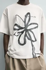 Camiseta de corte relajado confeccionada en algodón, con cuello redondo y manga corta. Presenta un estampado artístico de una flor a trazo grueso en color negro sobre fondo blanco.