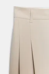 Pantalón de tiro medio color marrón, con pinzas en el delantero, perneras anchas de corte recto y trabillas para cinturón. Cuenta con bolsillos laterales y traseros, y cierre frontal con cremallera y botón.