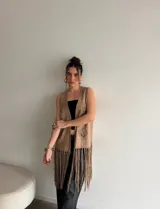 Chaleco de símil gamuza color beige, sin mangas, con detalles de tejido tipo crochet y flecos largos en el ruedo.