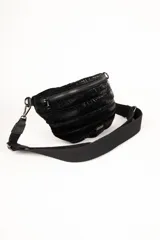 Cartera tipo riñonera acolchada, color negro brillante, con costuras horizontales y correa de tela ancha ajustable.