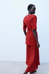 Vestido largo de punto color rojo, con cuello redondo, escote en V y manga corta. Presenta cierre frontal de botones a tono y una falda inferior de tejido combinado plisado.