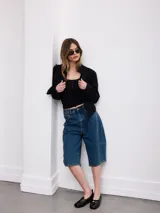 Chaqueta corta negra de gabardina con detalles de cordones decorativos bordados en el frente y bordes deshilachados.