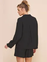 Blusa Allie Rose de color negro, corte holgado con escote en V cruzado y cuello camisero. Presenta mangas largas amplias con puños sutilmente fruncidos y diseño de silueta fluida.