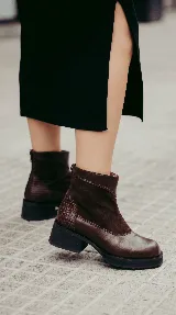 Bota corta de cuero negro con diseño de paneles que combina cuero liso y gamuza. Presenta puntera cuadrada, cierre trasero y suela con plataforma y taco bajo geométrico.