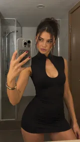Vestido corto negro ajustado, sin mangas, con cuello alto mao y abertura frontal tipo gota en el pecho.