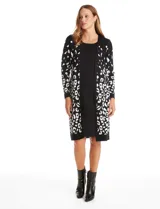 Vestido midi de tejido de punto con diseño integrado que simula un conjunto de vestido y cárdigan. Presenta un color base negro con detalles geométricos en blanco en las mangas y el ruedo. Posee escote redondo y mangas largas.