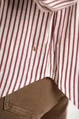 Camisa de corte oversize con estampado de rayas verticales, cuello clásico, cierre frontal con botones y bolsillo en el pecho. Presenta mangas largas con puños abotonados y un diseño fluido.